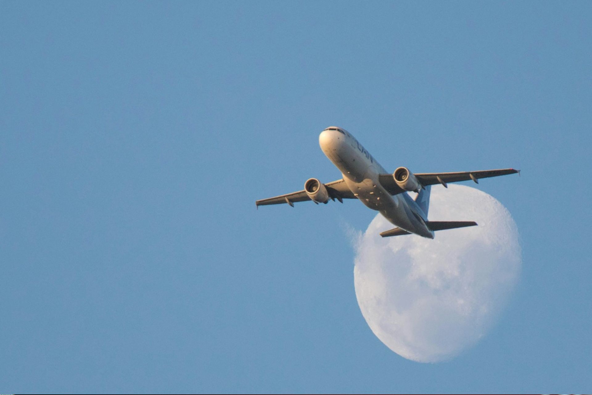 A plane in flight with the moon in the background
