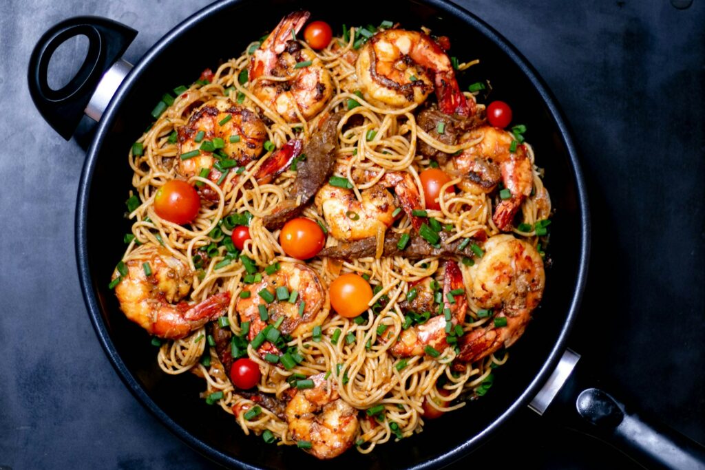 A pan of stir fry noodles with prawns and tomatoes