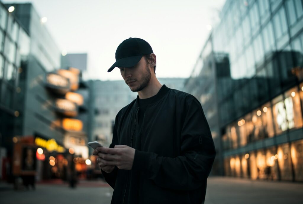A man in a black cap holding a phone in the street