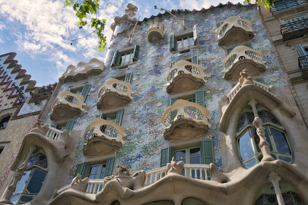 The front entrance of Casa Batlló, Barcelona. A bright exterior, with bone-like fences and curved windows.