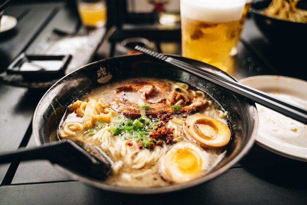 a bowl of ramen with chopsticks and a glass of beer
