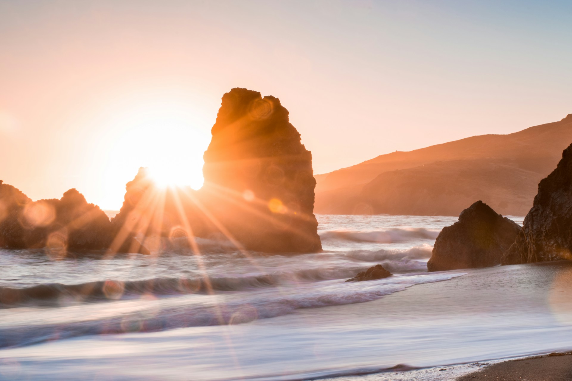 sun setting through rock on a beach