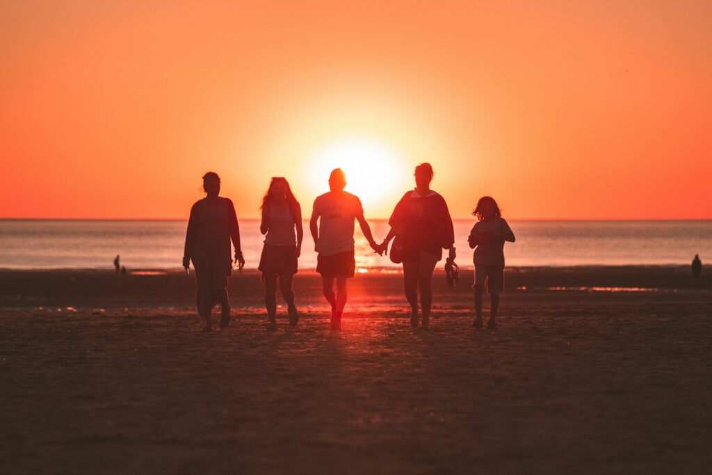 A family walking along a beach towards a sunset