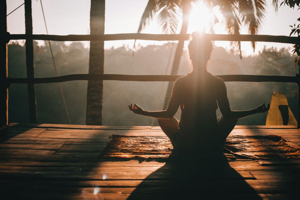 A woman meditating towards a sunset on a wooden balcony